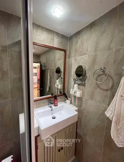 Compact bathroom with modern sink and mirror, featuring tiled walls and ceiling light.