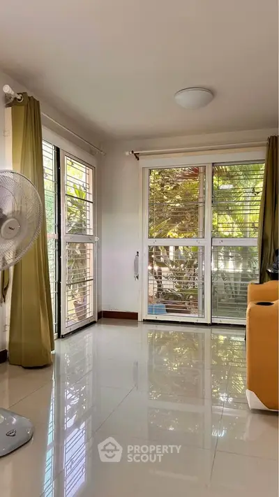 Bright living room with large windows and garden view, featuring modern decor and natural light.