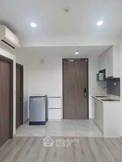 Modern apartment interior with sleek kitchen and compact fridge, featuring wood accents and bright lighting.