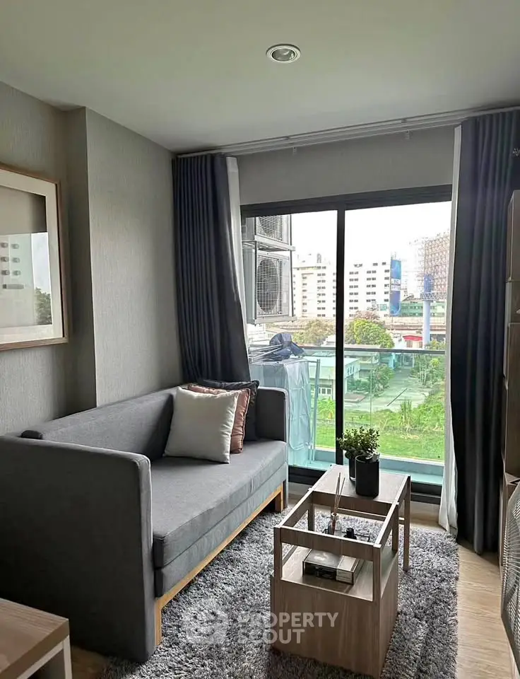 Modern living room with gray sofa, stylish decor, and city view from balcony.