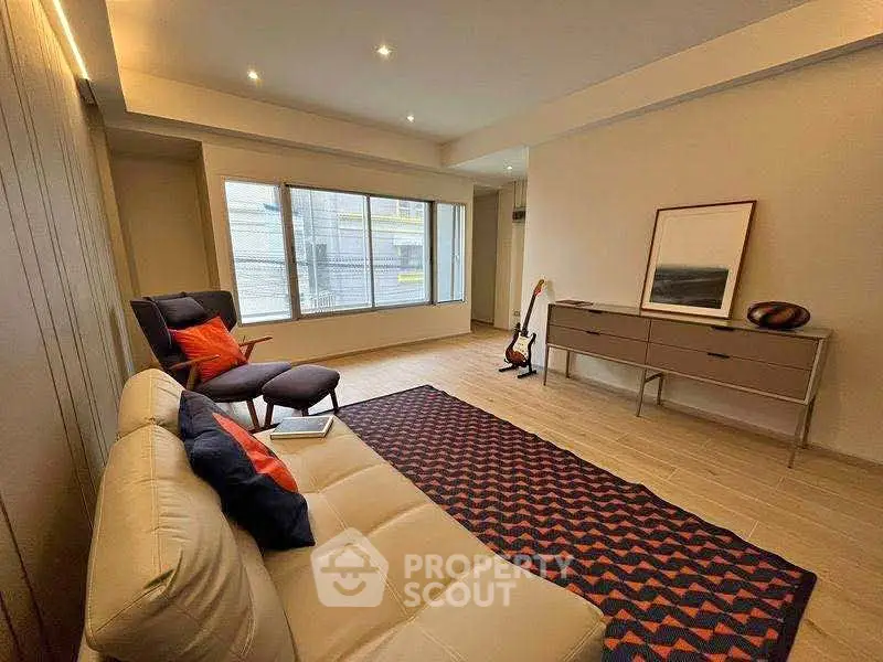 Modern living room with stylish decor, featuring a cozy sofa, armchair, and large window for natural light.