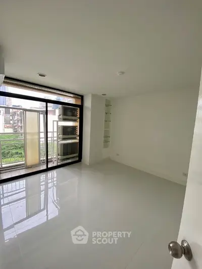 Spacious minimalist room with large windows and balcony access in modern apartment.