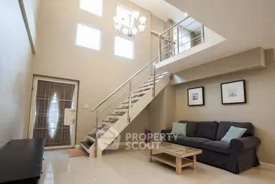 Spacious modern living room with high ceiling and mezzanine, featuring elegant staircase and cozy seating area.