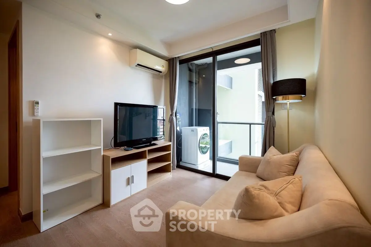 Modern living room with balcony and washing machine, featuring a cozy sofa and flat-screen TV.