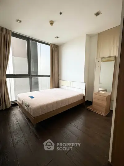 Spacious bedroom with large window and modern furnishings in a high-rise apartment.