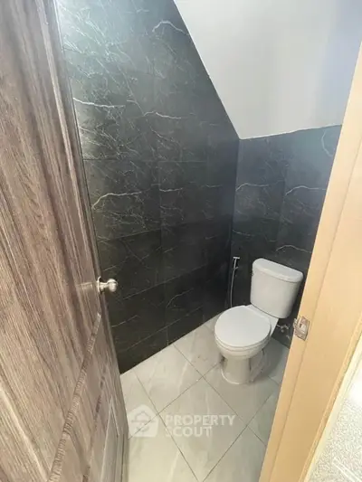 Compact modern bathroom with sleek dark tiles and white toilet.