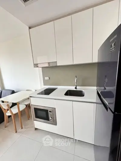 Modern kitchen with sleek white cabinets, built-in microwave, and Samsung fridge in a cozy apartment.