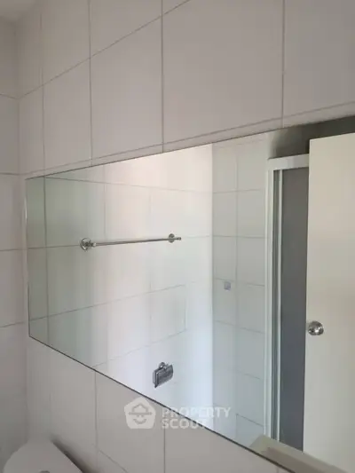 Modern bathroom with large mirror and shower enclosure, featuring sleek white tiles.