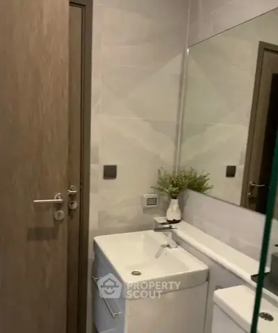 Modern bathroom with sleek sink and large mirror, featuring minimalist design and neutral tones.