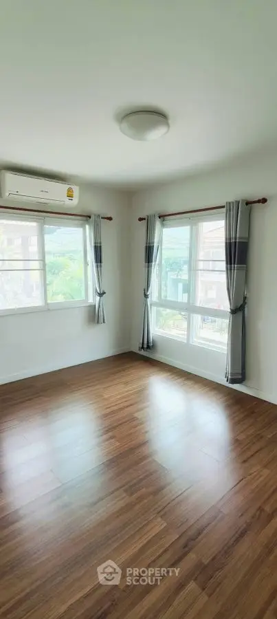 Bright empty room with wooden floors and large windows, perfect for customization.