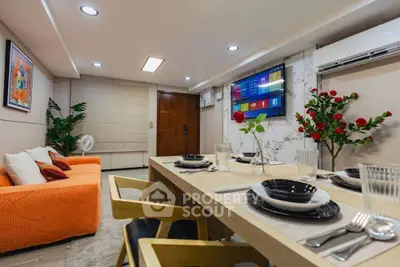 Modern living room with vibrant orange sofa, elegant dining setup, and wall-mounted TV in a stylish apartment.