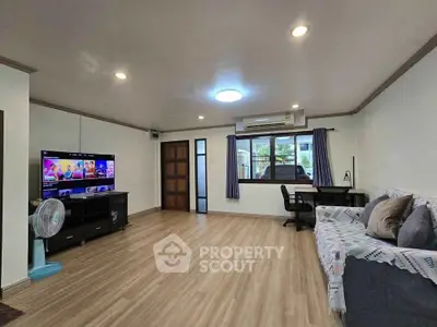 Spacious living room with modern decor and entertainment setup, featuring wooden flooring and ample natural light.