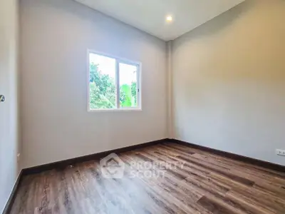 Spacious empty room with wooden flooring and large window offering natural light.