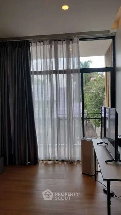 Modern living room with large window and balcony view, featuring sleek furniture and natural light.