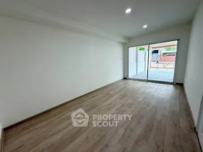 Spacious empty room with wooden flooring and large sliding glass doors leading to a patio.