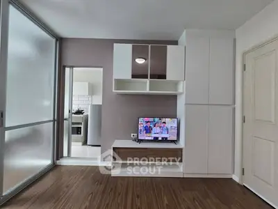 Modern living room with sleek cabinetry and TV, adjacent to a stylish kitchen.