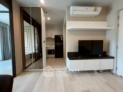 Modern living room with sleek design, featuring a wall-mounted TV and air conditioning, adjacent to a compact kitchen.