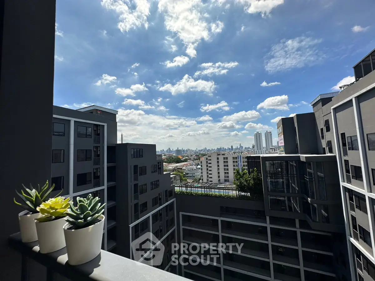 Stunning cityscape view from modern apartment balcony with potted plants and clear blue sky.