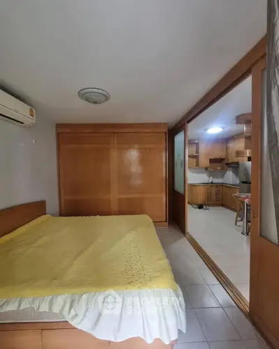 Cozy bedroom with wooden accents and open kitchen layout in modern apartment.