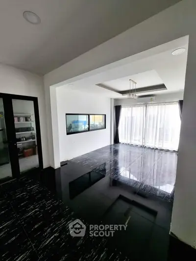 Spacious modern living room with glossy black tile flooring and large windows for natural light.