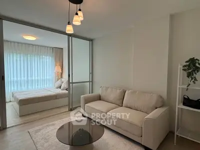 Modern living room with cozy sofa and stylish bedroom separated by glass doors.