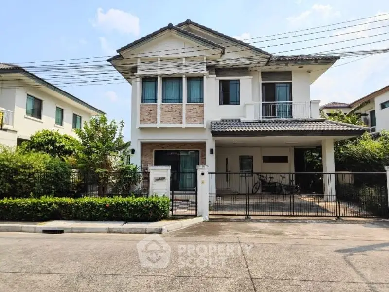 Charming two-story house with gated driveway and lush greenery in a serene neighborhood.