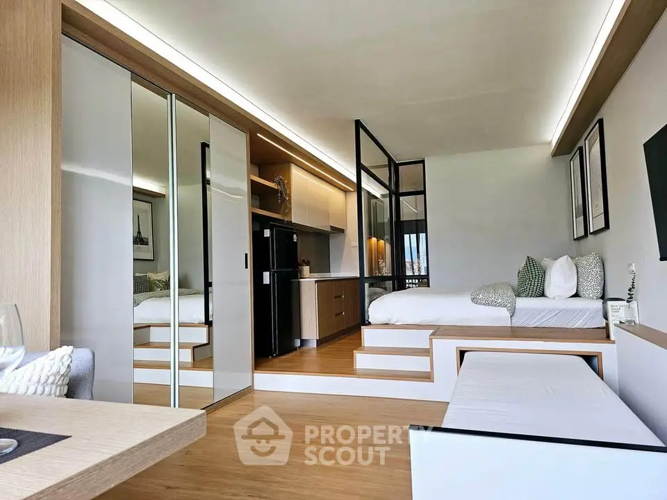 Modern studio apartment with elevated bed, sleek kitchen, and mirrored closet doors.