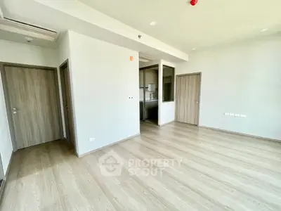 Spacious modern apartment interior with sleek wooden flooring and neutral walls, featuring multiple doors and natural light.