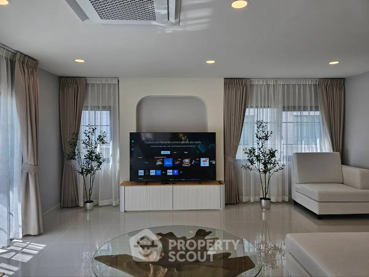 Modern living room with sleek decor, large TV, and natural light from floor-to-ceiling windows.