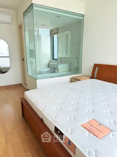 Modern bedroom with glass-enclosed bathroom and city view, featuring wooden flooring and stylish furnishings.