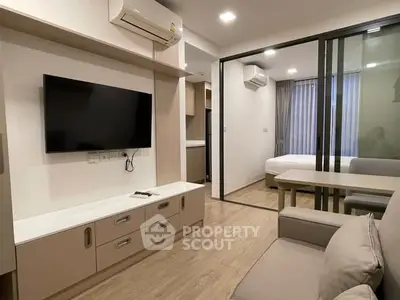 Modern apartment interior with open living room and bedroom, featuring sleek furniture and a large TV.