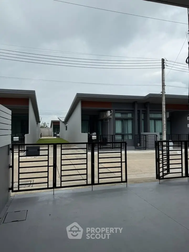 Modern single-story homes with sleek design and gated entrance under cloudy sky.