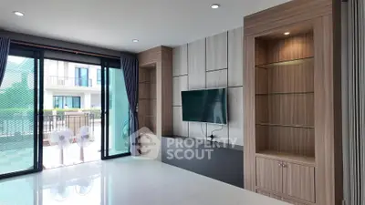 Modern living room with built-in shelves and large TV, overlooking balcony.