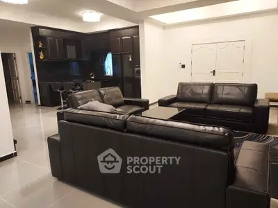 Luxurious modern living room with sleek black leather sofas and open kitchen layout.