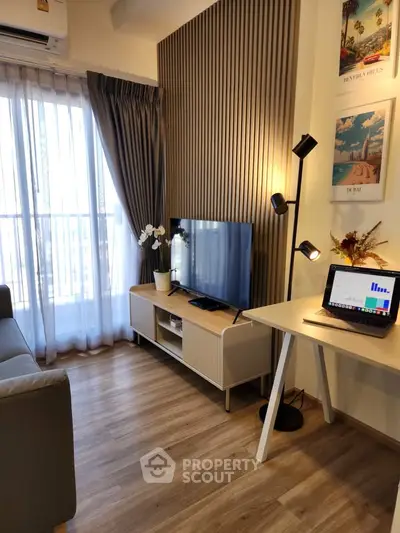 Modern living room with stylish decor, TV, and workspace near a large window with natural light.