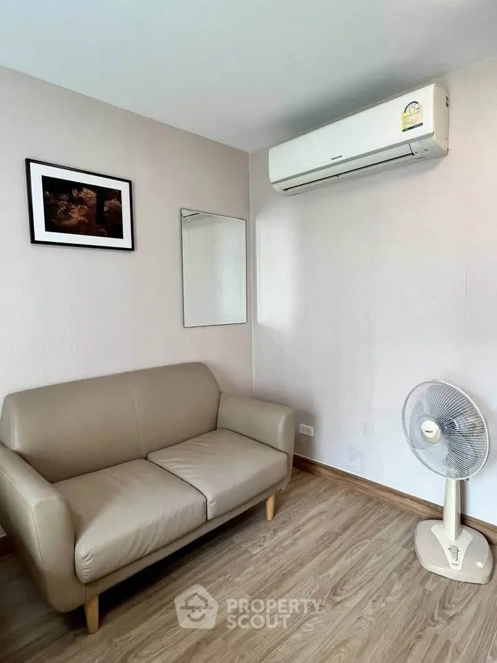 Cozy living room with beige sofa, wall-mounted air conditioner, and wooden flooring.