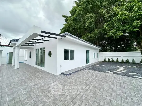 Modern white single-story house with spacious tiled patio and lush greenery.