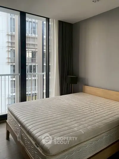 Modern bedroom with large windows and minimalist decor in urban apartment.