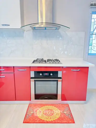 Modern kitchen with red cabinets and built-in oven, featuring a sleek gas stove and stylish backsplash.
