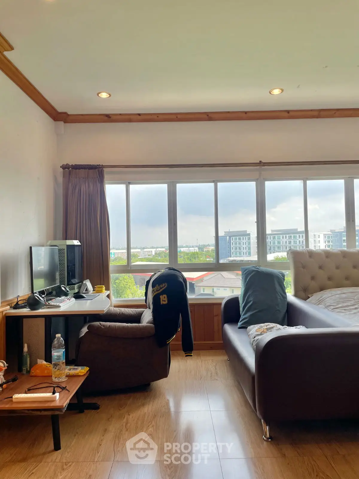 Cozy living room with large windows offering a scenic city view, featuring a comfortable sofa and work desk.