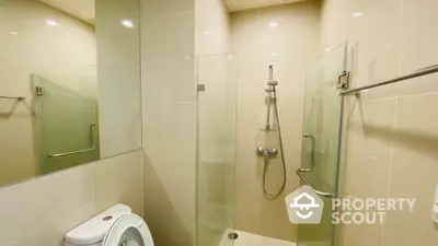 Modern bathroom with glass shower enclosure, beige tiles, and sleek fixtures offering a clean and minimalist appeal.