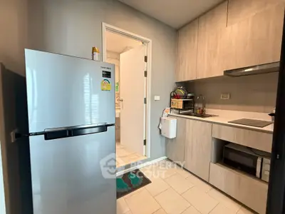 Modern kitchen with sleek appliances and wooden cabinetry, featuring a stainless steel fridge and compact design.