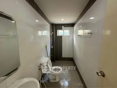 Modern bathroom with sleek tiles and natural light from small windows.