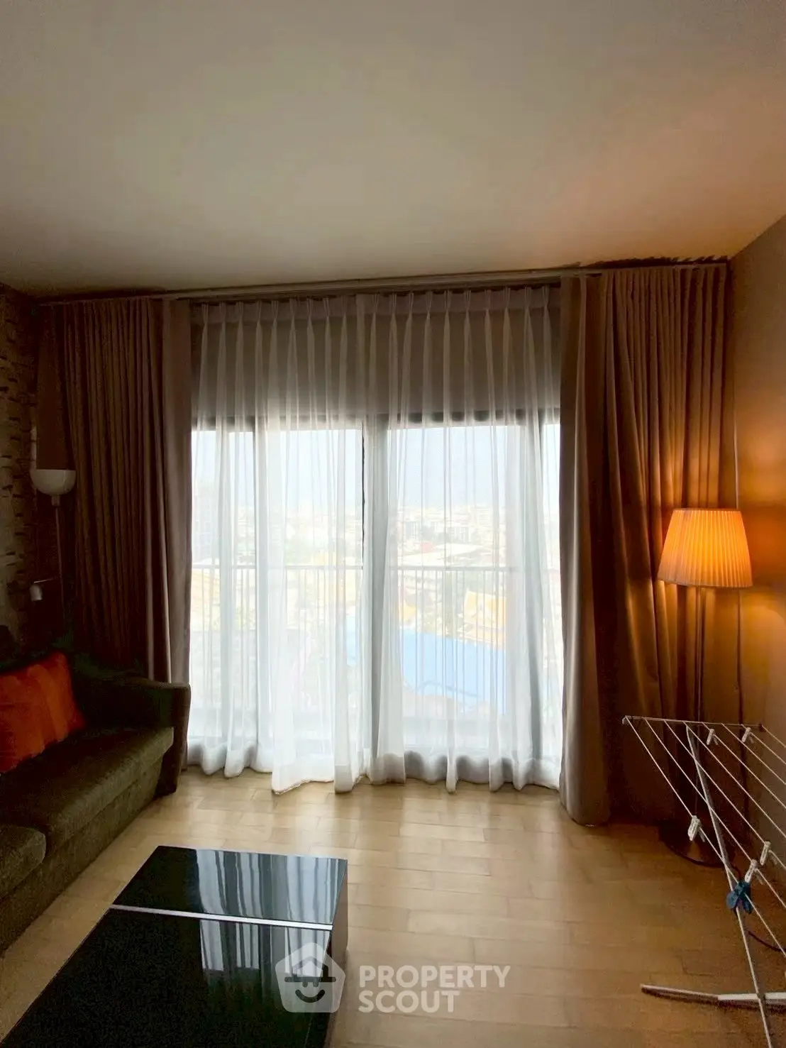 Cozy living room with floor-to-ceiling windows and elegant curtains, featuring a modern sofa and stylish lamp.