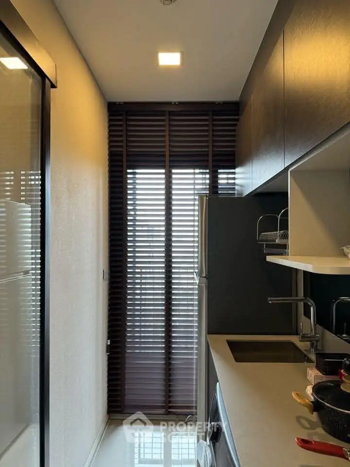 Modern kitchen with sleek cabinetry and natural light through window blinds.