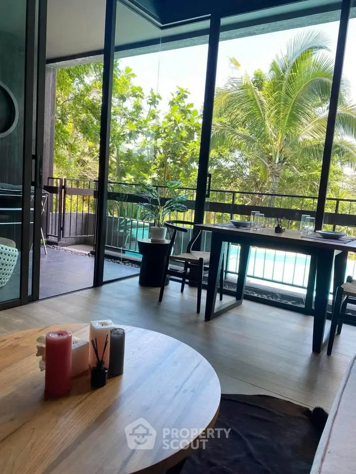 Spacious living room with large windows overlooking lush greenery and pool, perfect for relaxation.