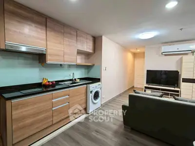 Modern open-layout kitchen and living room with sleek wooden cabinets and washing machine.