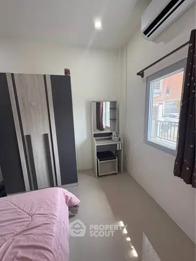 Cozy bedroom with modern wardrobe and vanity, featuring natural light from window and air conditioning.