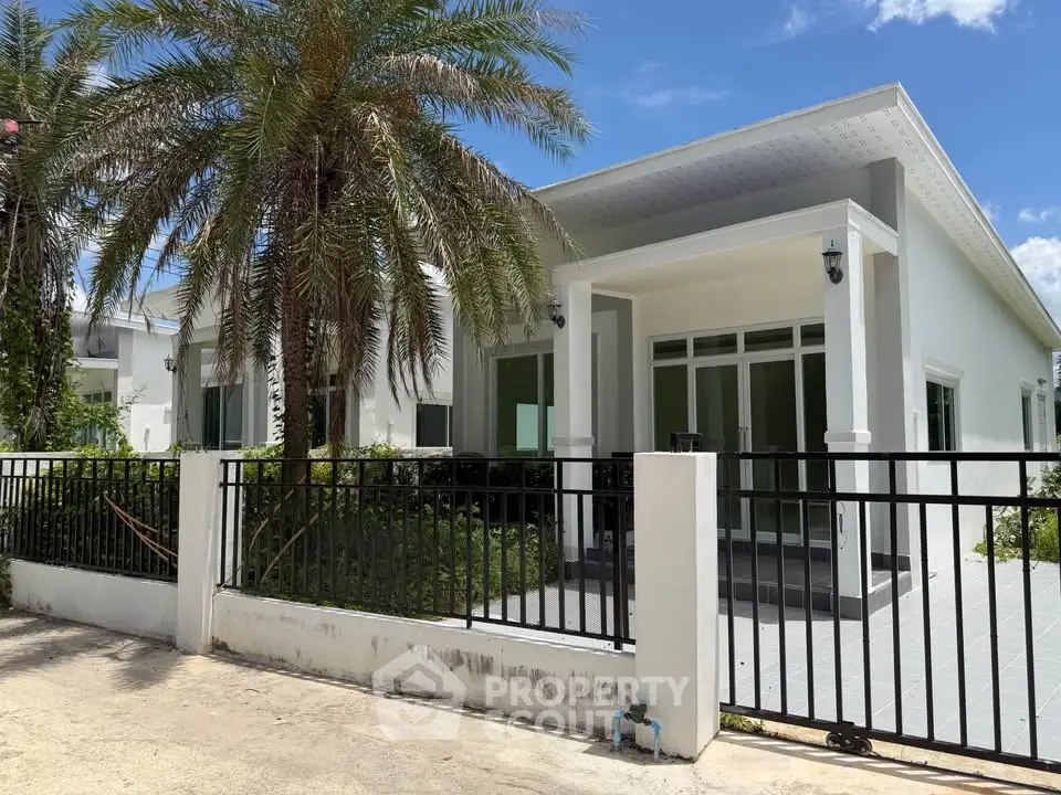 Charming modern house with lush palm tree and sleek fence, perfect for tropical living.