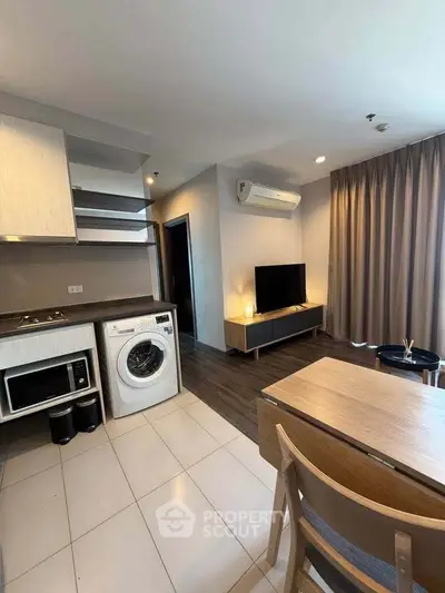 Modern apartment interior with kitchen and living area featuring washing machine and TV setup.